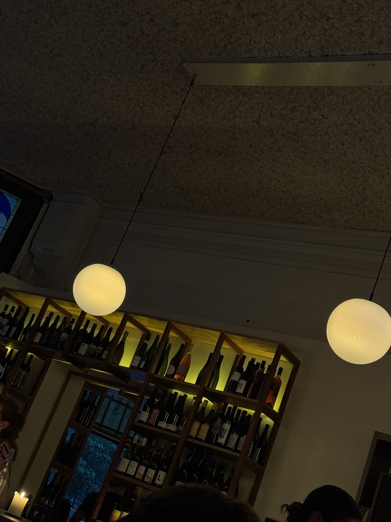 Barra y estantes con botellas y lámparas redondas de Café Binnenvisser.