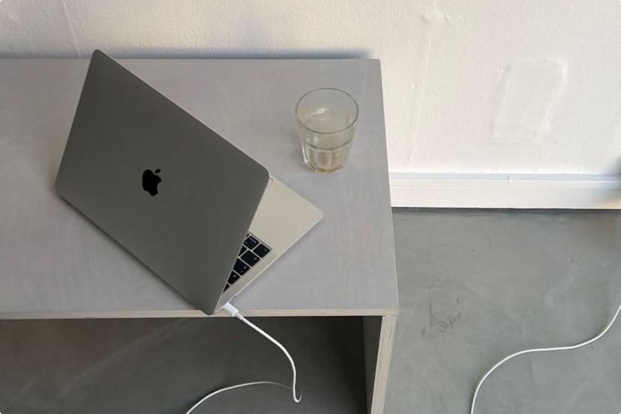 Portátil sobre una mesa clara junto a un vaso y un cable.
