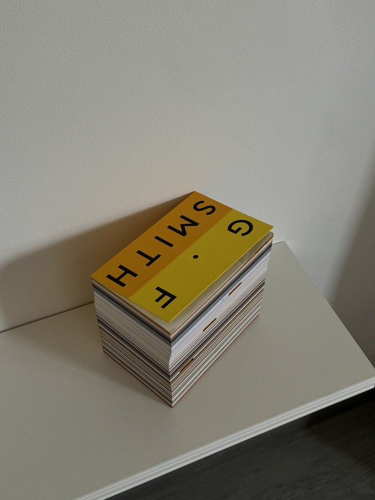 Pila de libros con una cubierta amarilla en una estantería blanca.