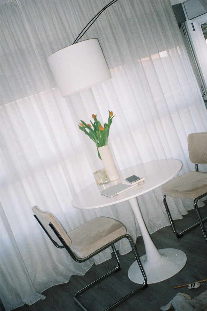 Mesa redonda con tulipanes delante de unas cortinas.