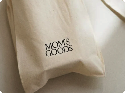 Bolsas de tela con cordón y logotipo negro de Mom’s Goods.