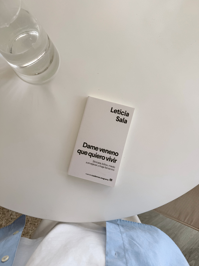 Un libro y un vaso de agua sobre una mesita blanca.