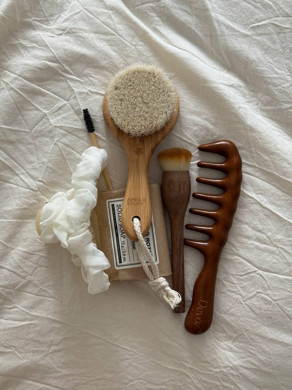 Cepillos de madera, peine y productos de cuidado sobre una tela blanca.