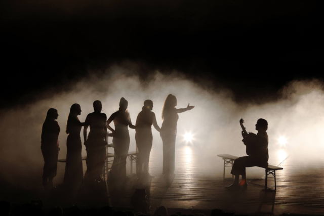 Escena flamenca a contraluz, con varias personas y un guitarrista.