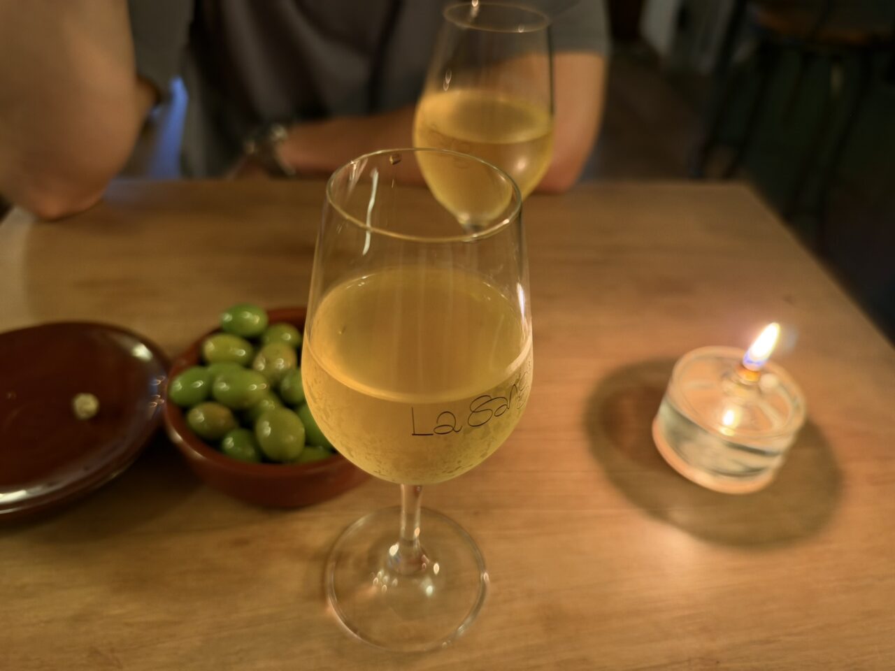 Dos copas de vino blanco, aceitunas y una vela sobre una mesa.