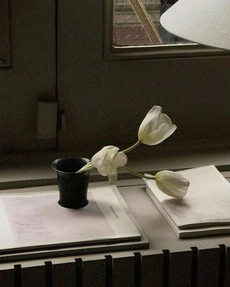 Tulipanes blancos en un pequeño jarrón junto a una ventana.
